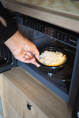 A hand places a bowl of food into the microwave.