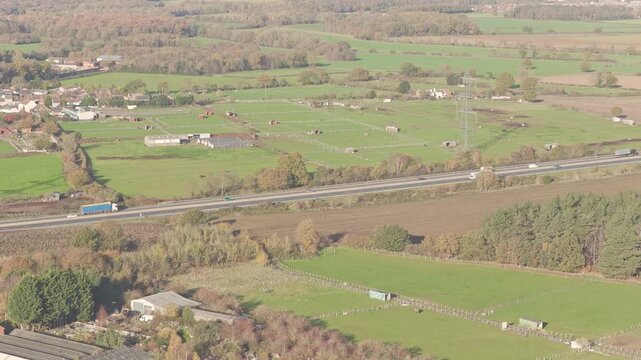 Aerial view of the M18 motorway cutting through green fields and scattered trees in Doncaster, South Yorkshire, showing cars, trucks and rural infrastructure from above