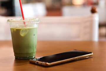 Relaxing iced matcha latte and smartphone on wooden cafe table. This refreshing green tea beverage offers quiet moment of calm during break from technology