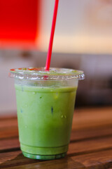 Refreshing iced matcha green tea latte beverage in clear plastic cup with red straw. Healthy delicious drink on wooden table inside modern cafe, moment of calm relaxation