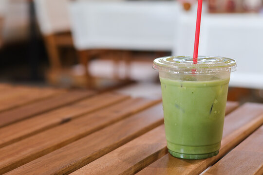 Refreshing iced matcha green tea latte in plastic cup with red straw. This cool beverage sits on wooden table at cafe, perfect drink for relaxing summer day