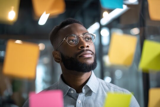 African American man in glasses thinking deeply surrounded by many vibrant sticky notes - Powered by Adobe