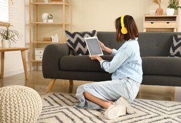 Young woman in headphones using blank tablet computer at home