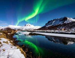 Emerald aurora borealis dances above snowy mountains and reflecting water