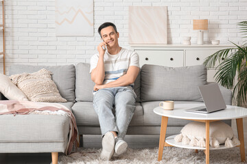 Handsome young man talking by mobile phone on sofa at home