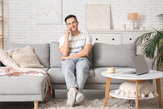 Handsome young man talking by mobile phone on sofa at home