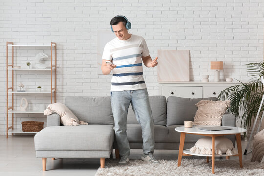 Handsome young man with modern mobile phone and headphones listening to music at home