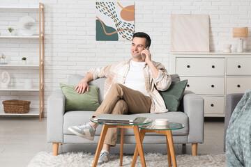 Handsome young man talking by mobile phone on sofa at home