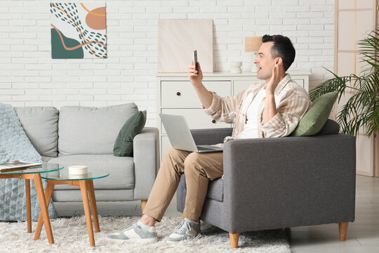 Handsome young man with laptop and modern mobile phone video chatting at home