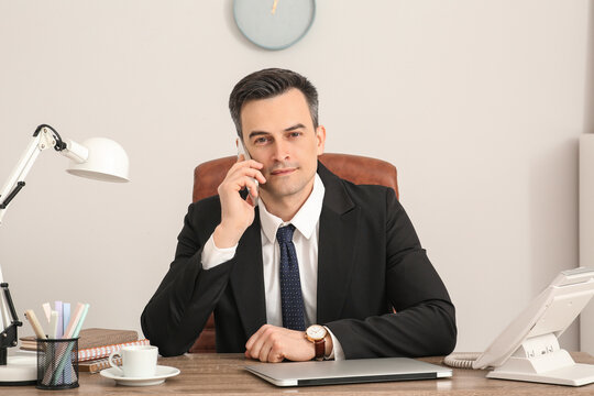 Handsome young businessman talking by modern mobile phone at table in office - Powered by Adobe