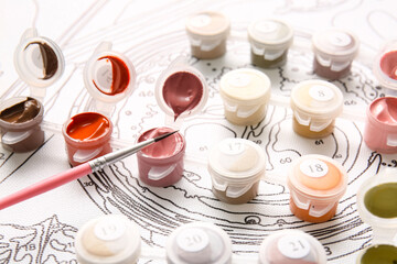 Paints and brush on unfinished canvas for painting by numbers, closeup