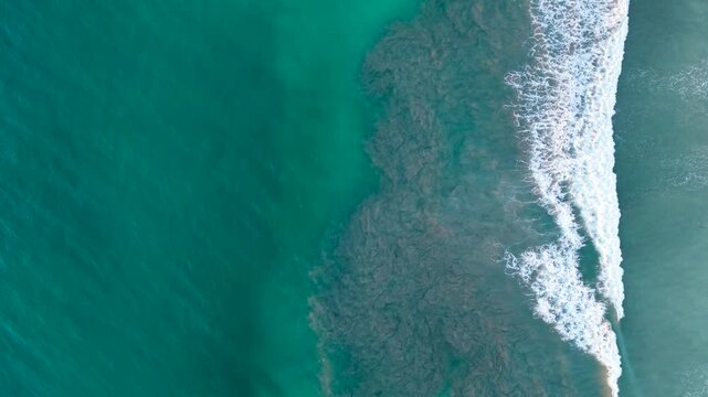 Stunning aerial top-down perspective of turquoise ocean water and powerful waves breaking along the coastline in avellanas beach, costa rica