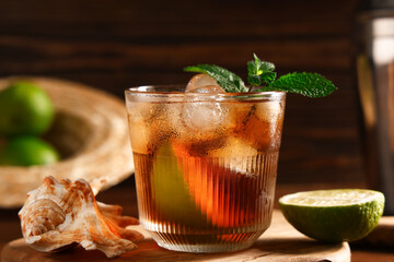 Glass of cold Cuba Libre cocktail with seashell on wooden background