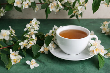 Cup of hot jasmine tea with flowers on green table