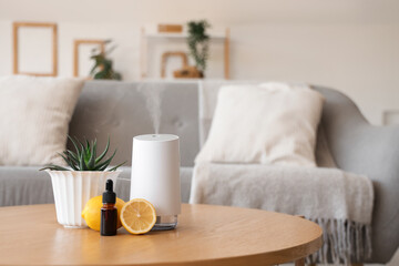 Air humidifier with essential oil, lemons and plant on table in living room, closeup