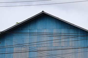 A weathered building with faded colored zinc walls stands behind a messy tangle of electrical...