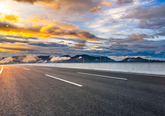 Naklejka premium Empty asphalt highway road and mountain with wind turbines landscape at dramatic sunrise