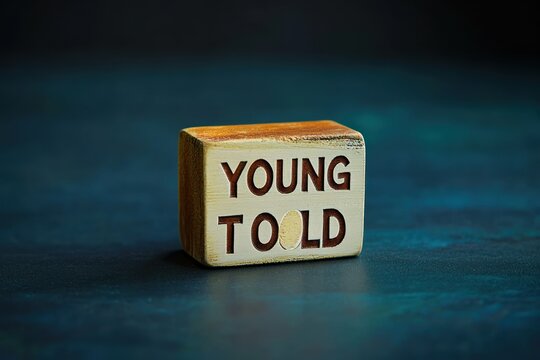Wooden block with engraved text transitioning from young to old representing aging and passage of time on dark background
