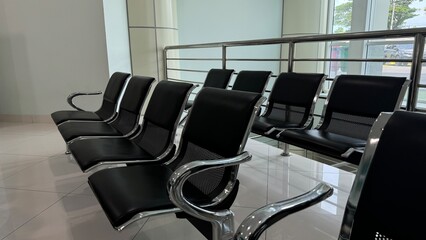 A row of empty, modern black tandem seating with chrome armrests in a bright