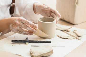 Young female potter shaping clay pot with wooden rib at table in home studio, closeup