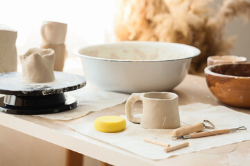 Clay cup and pottery tools on table in home studio, closeup