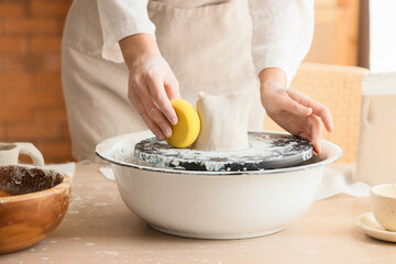 Female potter with sponge shaping clay on pottery wheel in home studio, closeup