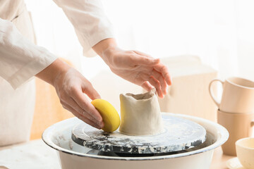 Female potter with sponge shaping clay on pottery wheel in home studio, closeup