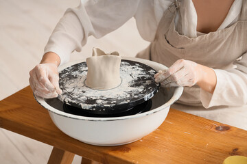 Young female potter cutting clay on pottery wheel in home studio, closeup