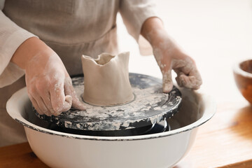 Young female potter cutting clay on pottery wheel in home studio, closeup