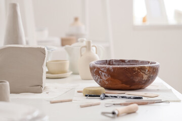 Clay block, bowl and pottery tools on table in home studio, closeup