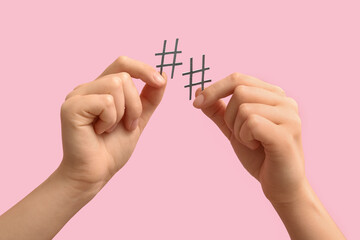 Female hands holding hashtags on pink background