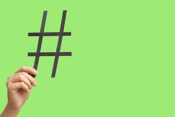 Female hand holding hashtag made of paper on green background