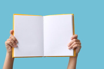 Hands of little girl holding open blank book on blue background