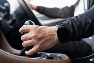 Close-up hand shifting gear with smartwatch while driving modern car, showing control, focus and lifestyle