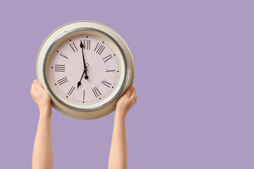 Female hands holding wall clock on lilac background © Pixel-Shot