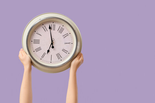 Female hands holding wall clock on lilac background