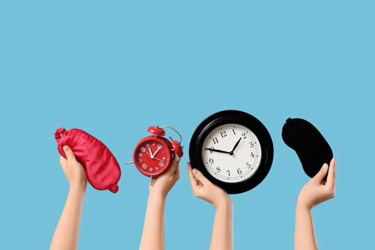 Female hands holding different clocks and sleep masks on blue background