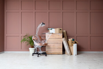 Office chair, standard lamp and chest of drawers wrapped in stretch film near brown wall