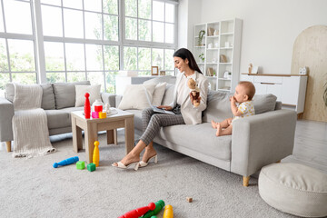 Young business mother working with laptop and cute little baby playing in living room