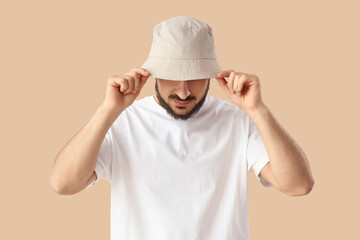 Handsome young man in stylish bucket hat on beige background