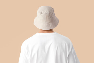 Handsome young man in stylish bucket hat on beige background, back view
