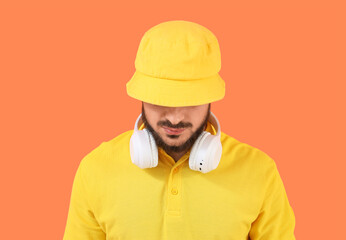 Handsome young man in stylish bucket hat and headphones on orange background