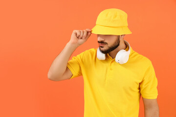 Handsome young man in stylish bucket hat and headphones on orange background