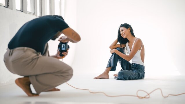 Photographer taking photos of a smiling model during a professional photoshoot in a bright studio