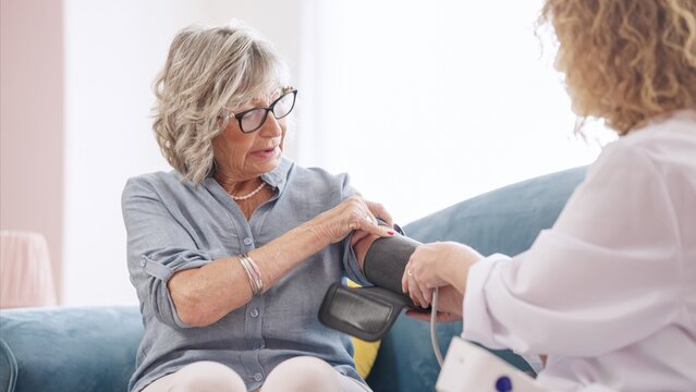 Female doctor is using a sphygmomanometer for measuring blood pressure of a senior woman during home visit