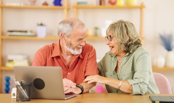 Happy senior couple sharing laughter while using a laptop together at home, enjoying moments of connection and joy in their cozy living room