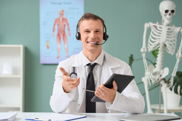 Young male doctor with tablet computer giving consultation online in clinic