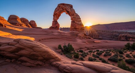 Delicate arch in arches national park utah at sunrise, showcasing the iconic sandstone formation glowing orange against a clear blue sky with sunburst