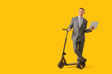 Young businessman with electric scooter and laptop on yellow background