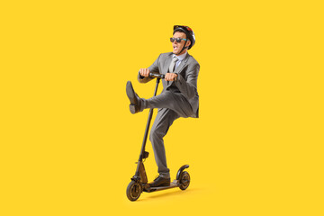 Funny young businessman riding electric scooter on yellow background